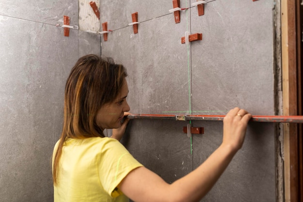 Mulher verificando se os ladrilhos de um canteiro de obras estão nivelados para garantir a qualidade de sua instalação com um piso nivelado à mão ou conceito de ladrilhos de casa