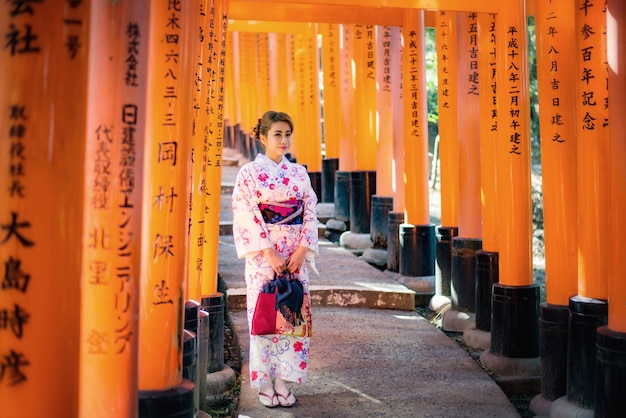 Mulher vestida com traje tradicional japonês passando sob os portões tori no santuário fushimi-inari, Kyoto, Japão