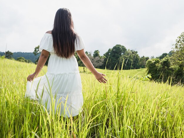 Mulher vestida de branco fica em um prado bela natureza com treevalley e céu nublado.