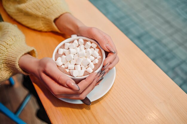 Mulher vestida de suéter quente, beba marshmallow com leite, café, cacau ou café com leite