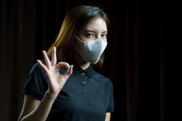 Mulher vestindo a máscara de proteção respiratória N95 mostrando sinal de mão ok.
