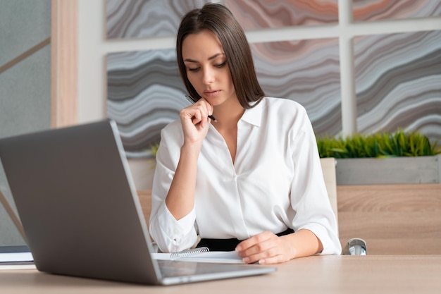 Mulher vestindo camisa branca sentada Mesa com laptop e notebook fazendo anotações Conceito de trabalho