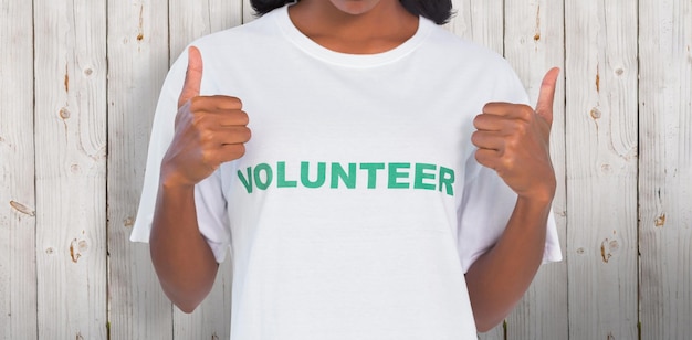 Mulher vestindo camiseta voluntária e levantando os polegares contra um fundo de madeira