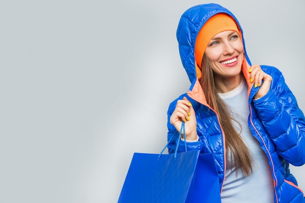 mulher vestindo casaco azul segurando sacolas de compras sobre fundo cinza