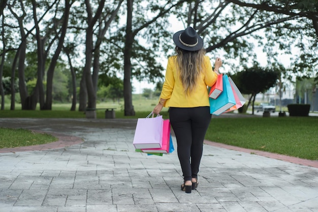 Foto mulher vestindo jaqueta amarela andando em um jardim com sacolas de compras multicoloridas conceito de compras