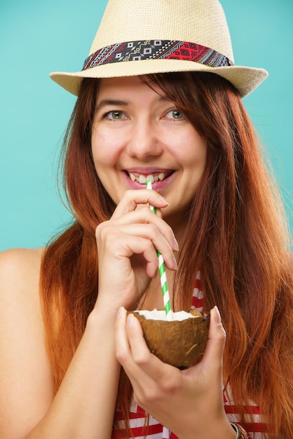 Mulher vestindo maiô e chapéu de palha bebe leite de coconaut sobre fundo turquesa colorido