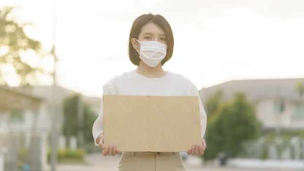 Mulher vestindo máscara segurando uma faixa em branco para colocar o texto em protestar.