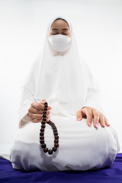 Mulher vestindo mukena rezando com contas de oração em fundo isolado