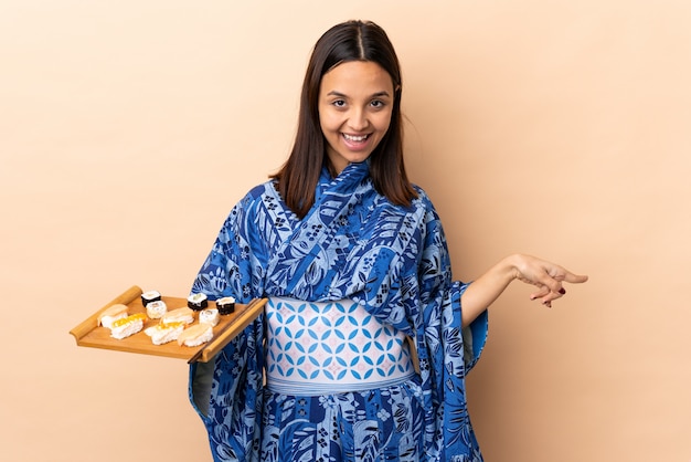 Mulher vestindo quimono e segurando sushi sobre dedo apontando isolado para as laterais e feliz