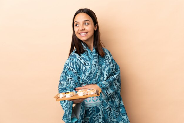 Mulher vestindo quimono e segurando sushi sobre fundo isolado, com os braços cruzados e feliz