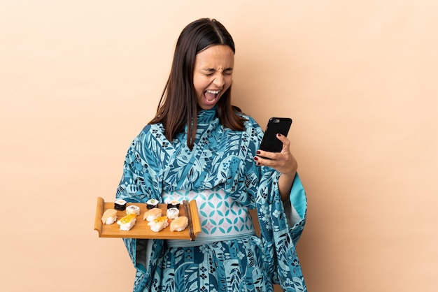 Mulher vestindo quimono e segurando sushi sobre parede com telefone em posição de vitória