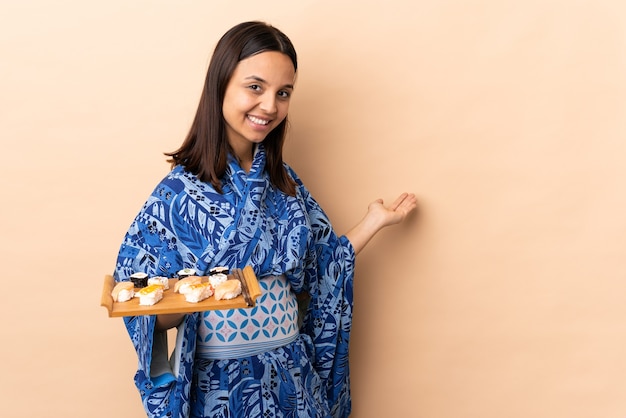 Mulher vestindo quimono e segurando sushi sobre uma parede isolada, estendendo as mãos para o lado para convidar para vir