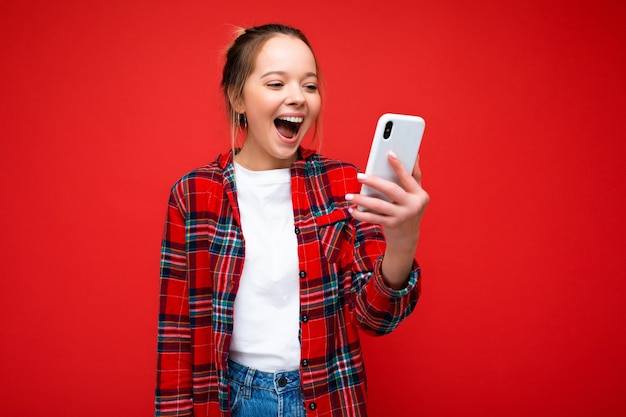 mulher vestindo roupas casuais elegantes, isolado na parede com espaço de cópia, segurando e usando o telefone celular, olhando para a tela do dispositivo.