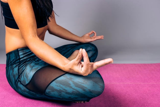 Mulher vestindo roupas esportivas sentada no chão em casa relaxa e faz o gesto de meditação com os dedos Conceito de ioga