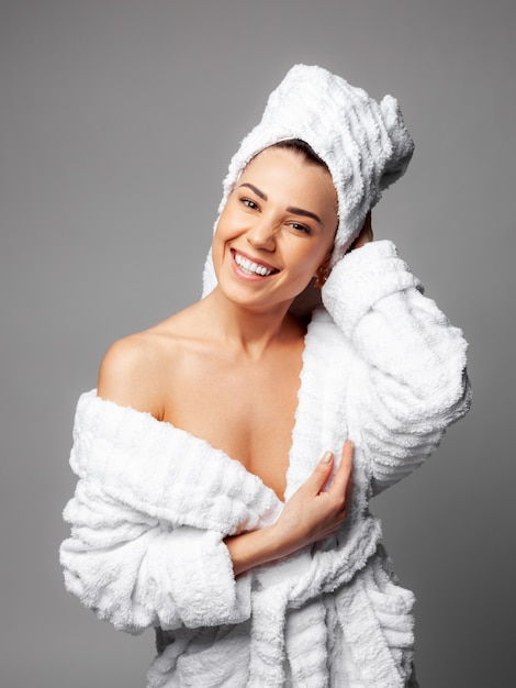 Mulher vestindo toalha branca na cabeça e roupão de banho branco, sorrindo