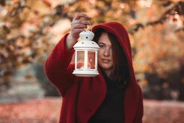 Mulher vestindo um casaco cor de vinho segurando lanterna na floresta de outono estilo vitoriano vintage