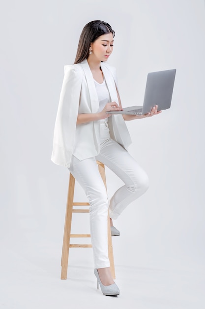 Mulher vestindo um terno branco sentada trabalhando através do computador isolado fundo branco