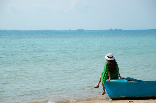 Mulher vestindo uma camisa verde, usando um chapéu branco, sentado em um barco estacionado na praia.
