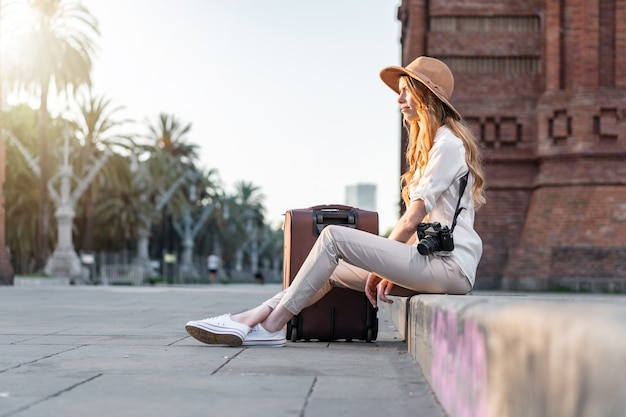 Mulher viajando e sentada na rua de Barcelona com uma mala e uma câmera de filme vintage.