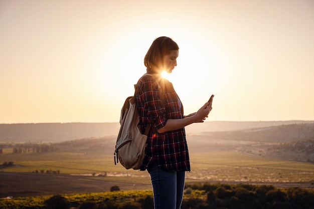 Mulher viajando muito em pé no topo da montanha ao pôr do sol e usando telefone celular