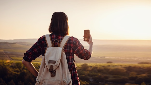 Foto mulher viajando muito em pé no topo da montanha ao pôr do sol e usando telefone celular