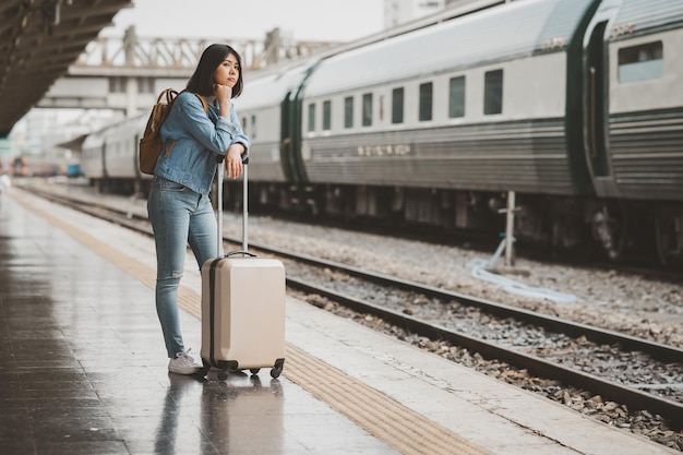 Mulher viajante asiática com bagagem sozinha esperando o trem na plataforma da estação ferroviária