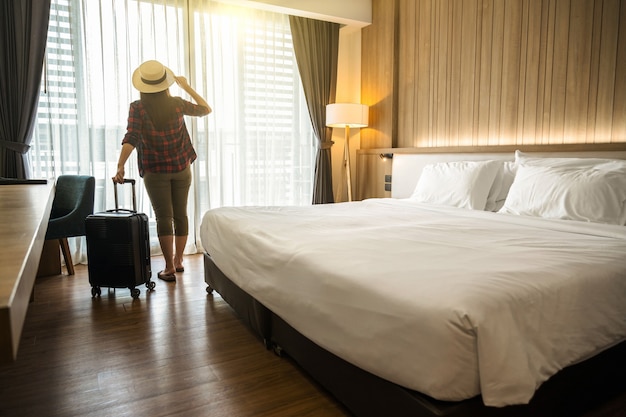 Foto mulher viajante asiática feliz em pé com bagagem em um quarto de hotel ou albergue