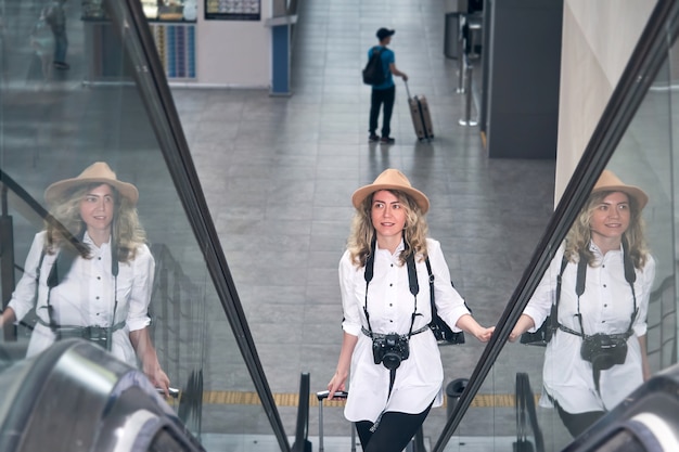 Mulher viajante com câmera sobe a escada rolante no aeroporto