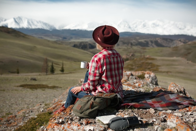 Mulher viajante com chapéu e caneca no fundo das montanhas