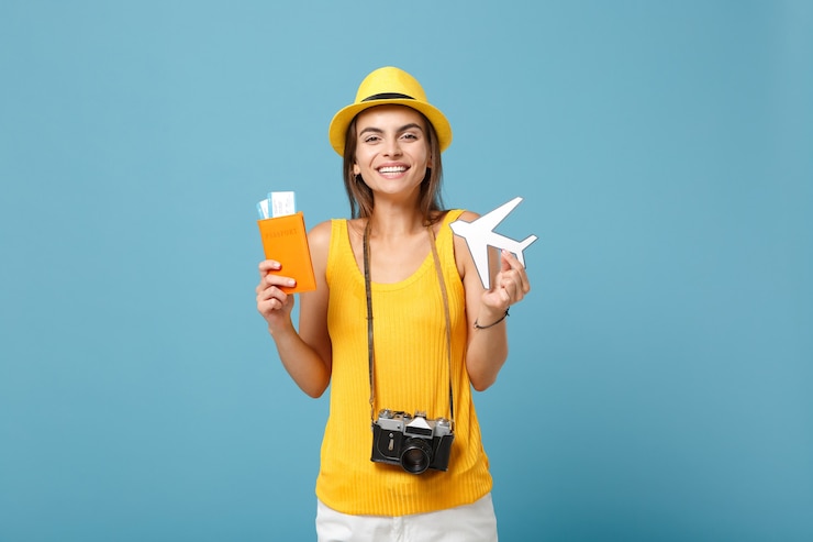 Foto mulher viajante com roupas casuais de verão amarelo e chapéu segurando a câmera de ingressos no azul