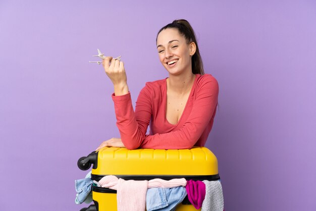 Mulher viajante com uma mala cheia de roupas isolado parede roxa