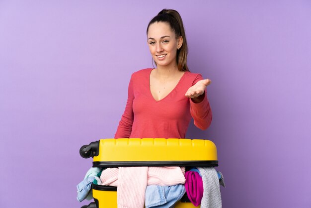 Mulher viajante com uma mala cheia de roupas sobre aperto de mão isolado parede roxa depois de bom negócio