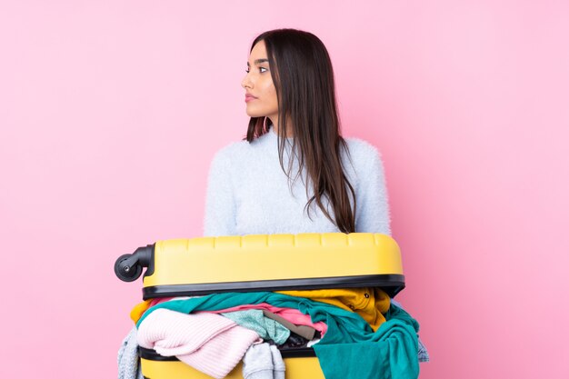 Mulher viajante com uma mala cheia de roupas sobre o lado olhando rosa