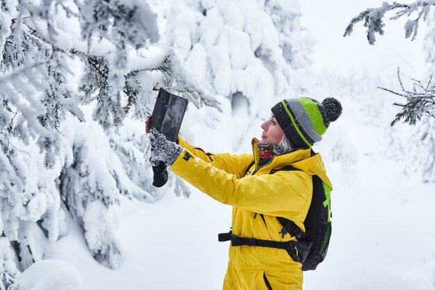 Mulher viajante com uma mochila em uma floresta de neve no inverno grava vídeo com ela mesma por smartphone