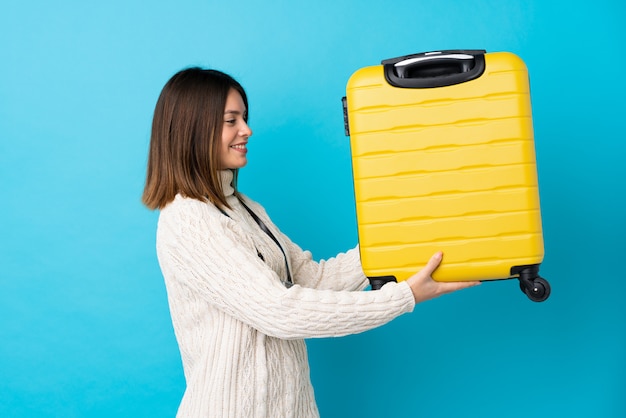 Foto mulher viajante segurando uma mala amarela sobre parede azul isolada