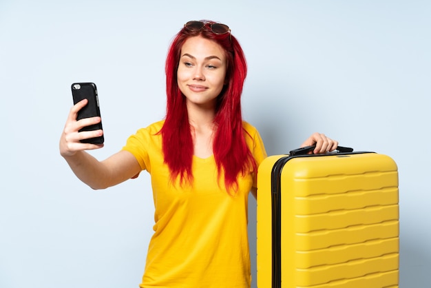 Mulher viajante segurando uma mala isolada na parede azul, fazendo um selfie