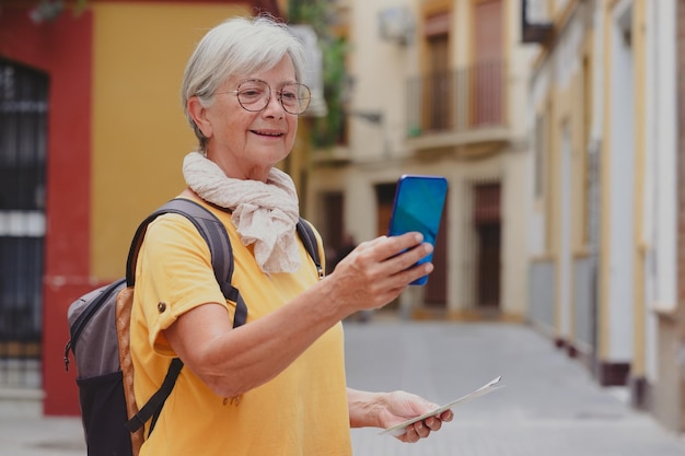 Mulher viajante sênior despreocupada carregando mochila visitando a cidade velha de Sevilha olhando para o telefone sorrindo senhora idosa curtindo viagens e descobertas