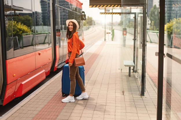 Foto mulher viajante sorridente embarcando em um bonde moderno na estação ao ar livre