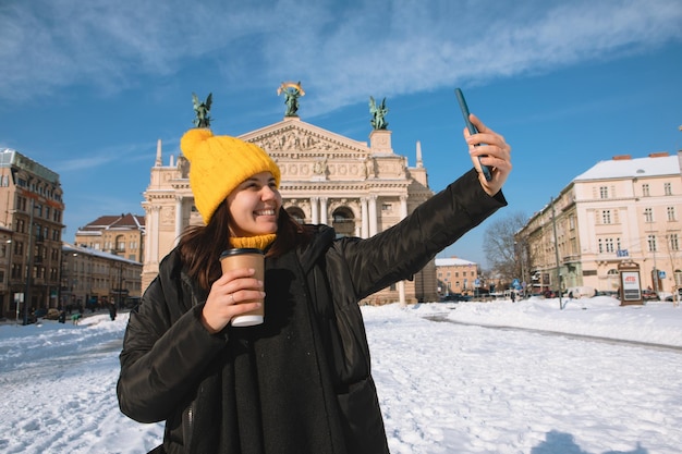 Mulher viajante tomando café para tirar selfie em frente ao prédio da ópera