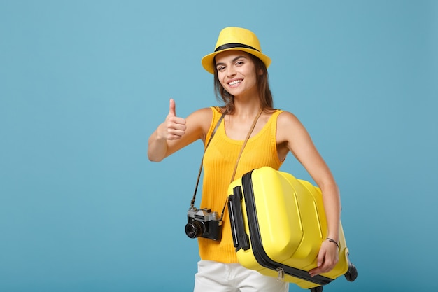 Mulher viajante turista em roupas casuais amarelas, chapéu com câmera fotográfica de mala em azul