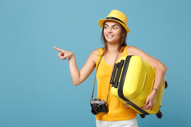 Mulher viajante turista em roupas casuais amarelas, chapéu com câmera fotográfica de mala em azul