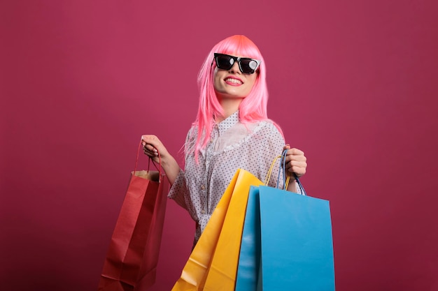 Mulher viciada em compras com óculos de sol carregando sacolas de compras depois de comprar roupas da loja de varejo no shopping, usando a compra com desconto de venda. Cliente elegante se sentindo feliz depois de pagar o dinheiro no pacote.