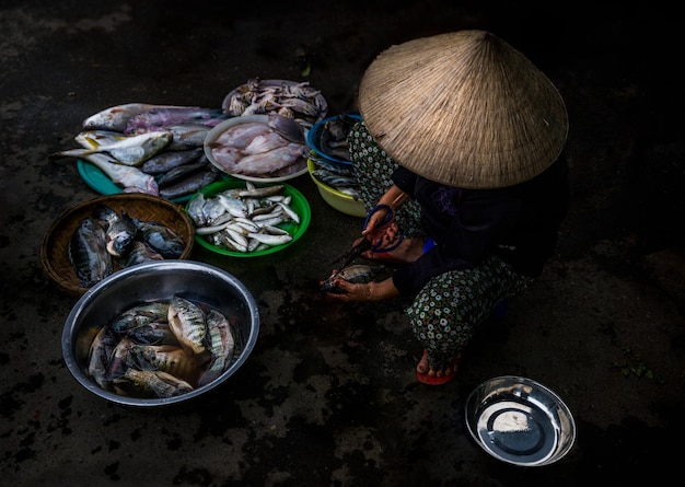 Mulher vietnamita limpando peixe para vender em um mercado público