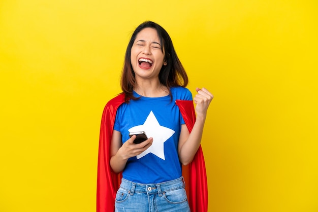 Mulher vietnamita super-herói isolada em fundo amarelo com telefone em posição de vitória