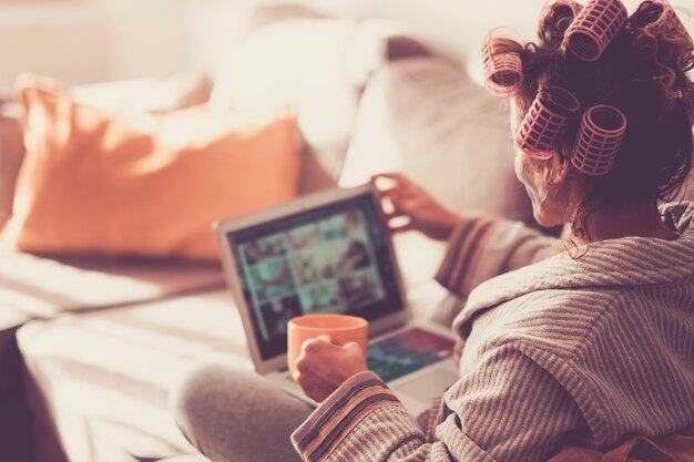 Foto mulher vista de costas usando um laptop de tecnologia moderna em casa enquanto tem rolos no cabelo encaracolado
