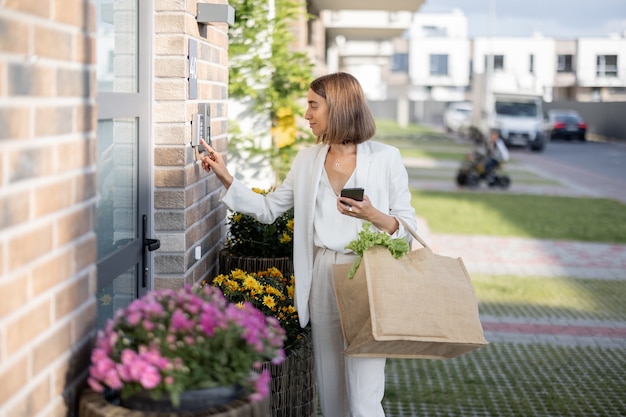 Mulher voltando para casa com mantimentos e digita um código para acessar a porta