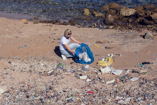 Mulher voluntária com um grande saco azul, coletando lixo na praia. conceito de poluição ambiental
