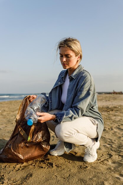 Foto mulher voluntária irritada está coletando resíduos plásticos na praia para contribuir com o esforço de manter a natureza limpa