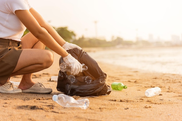 Mulher voluntária pegando garrafa de plástico em saco plástico de lixo preto para limpar a praia