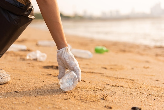 Mulher voluntária pegando garrafa de plástico em saco plástico de lixo preto para limpar a praia